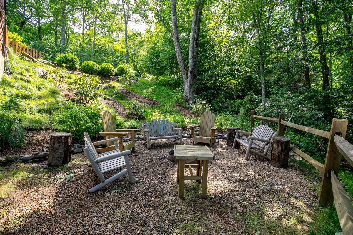 A cozy outdoor seating area with wooden chairs and a small table surrounded by dense greenery, ideal for gathering around a fire pit, sharing stories, or enjoying meals under the open sky.