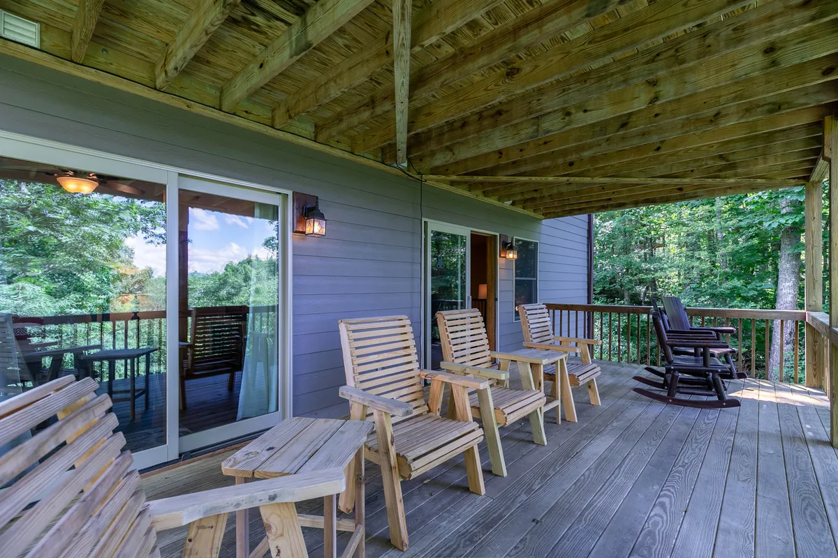 An exterior view showcasing wooden rocking chairs and patio seating, enveloped by lush greenery. The setting is tranquil yet social, ideal for gathering with friends outdoors, enjoying coffee in the morning, or winding down after a night out.