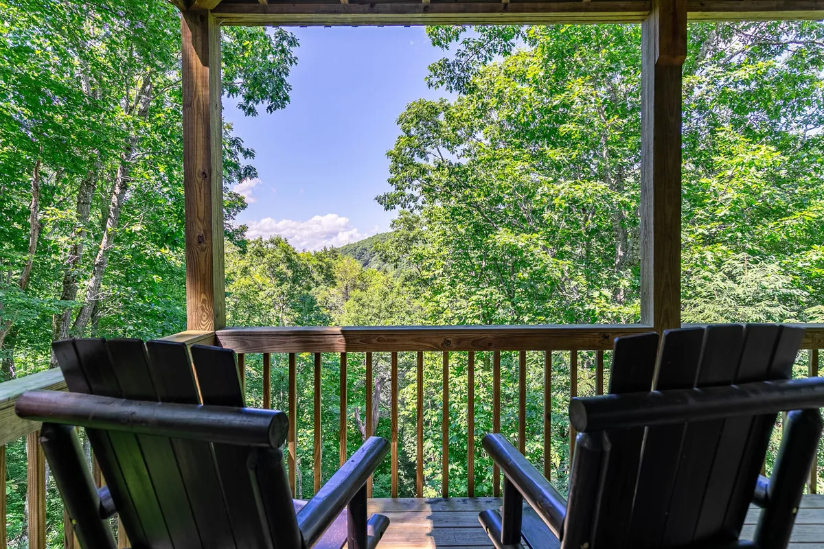 Wooden rocking chairs on a porch overlook lush greenery and a panoramic mountain view. The space is perfect for relaxing, stargazing, or recounting the day's adventures with friends and family.