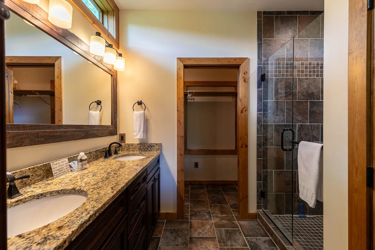A modern bathroom featuring a vanity with dual sinks, a large glass shower, and warm wooden accents. The space feels luxurious, bright, and designed for both convenience and self-care.