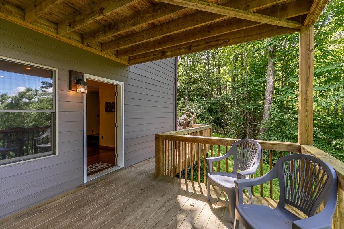 A tranquil deck featuring comfortable chairs and surrounded by trees, with an inviting doorway leading back into the home—an ideal setting for relaxing after a day of exploring local attractions.