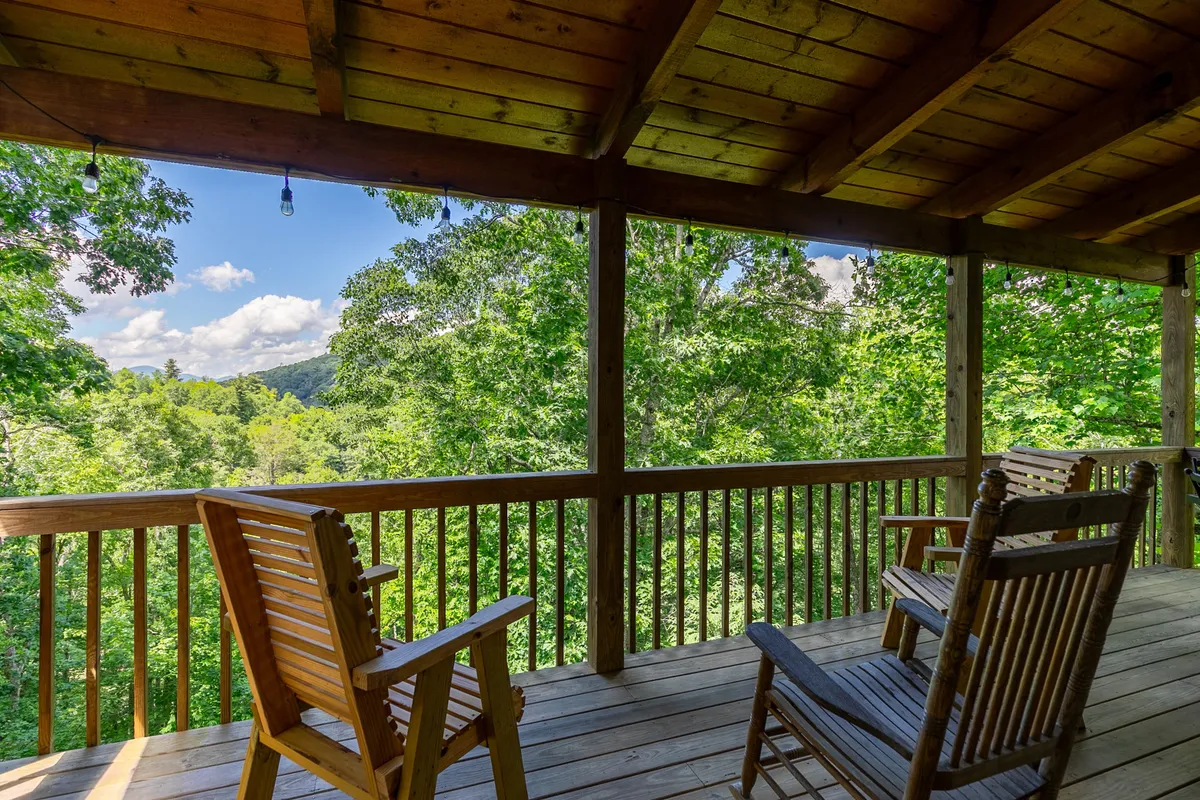 A detailed look at a deck with classic wooden rocking chairs set against a backdrop of verdant trees and distant mountains. The area exudes tranquility and encourages relaxation while offering a taste of the fresh Blue Ridge air.